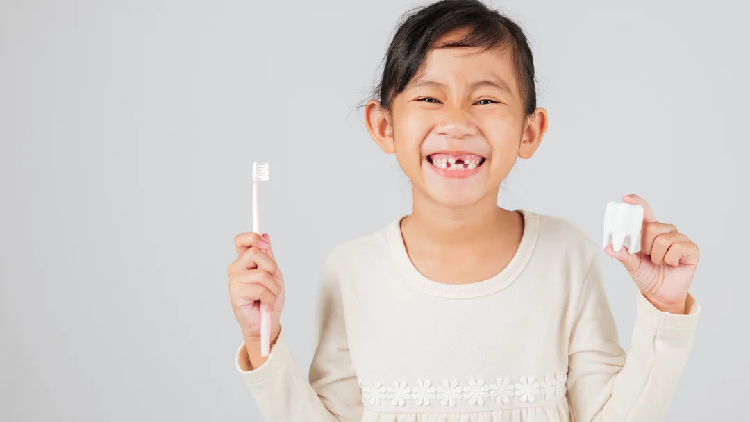 A young patient smiling at Tomorrow’s Dentistry, holding a toothbrush and a model tooth